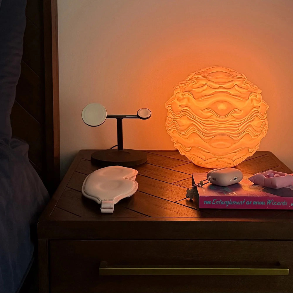 Noctis Studio Syzygy Lamp resting on a bed, featuring a sleek, modern design with a curved arm and soft lighting.