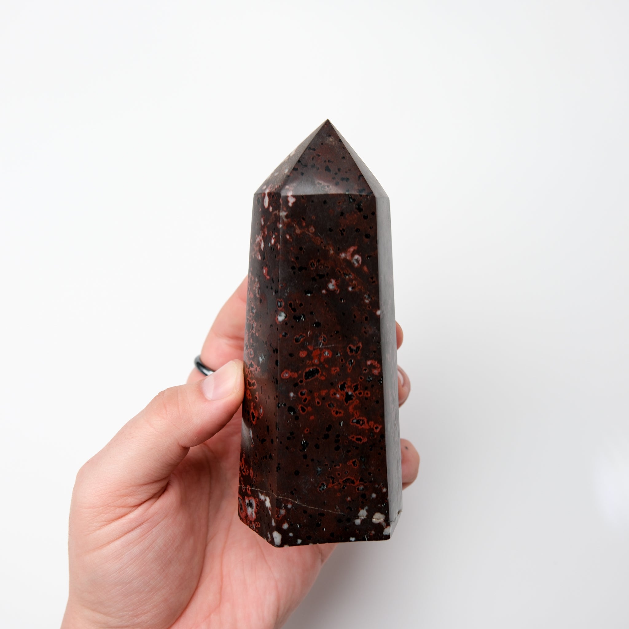 Cinnabar Peridotite pillar sculpture by Noctis Studio, showing a tall, textured stone pillar with reddish and greenish hues.