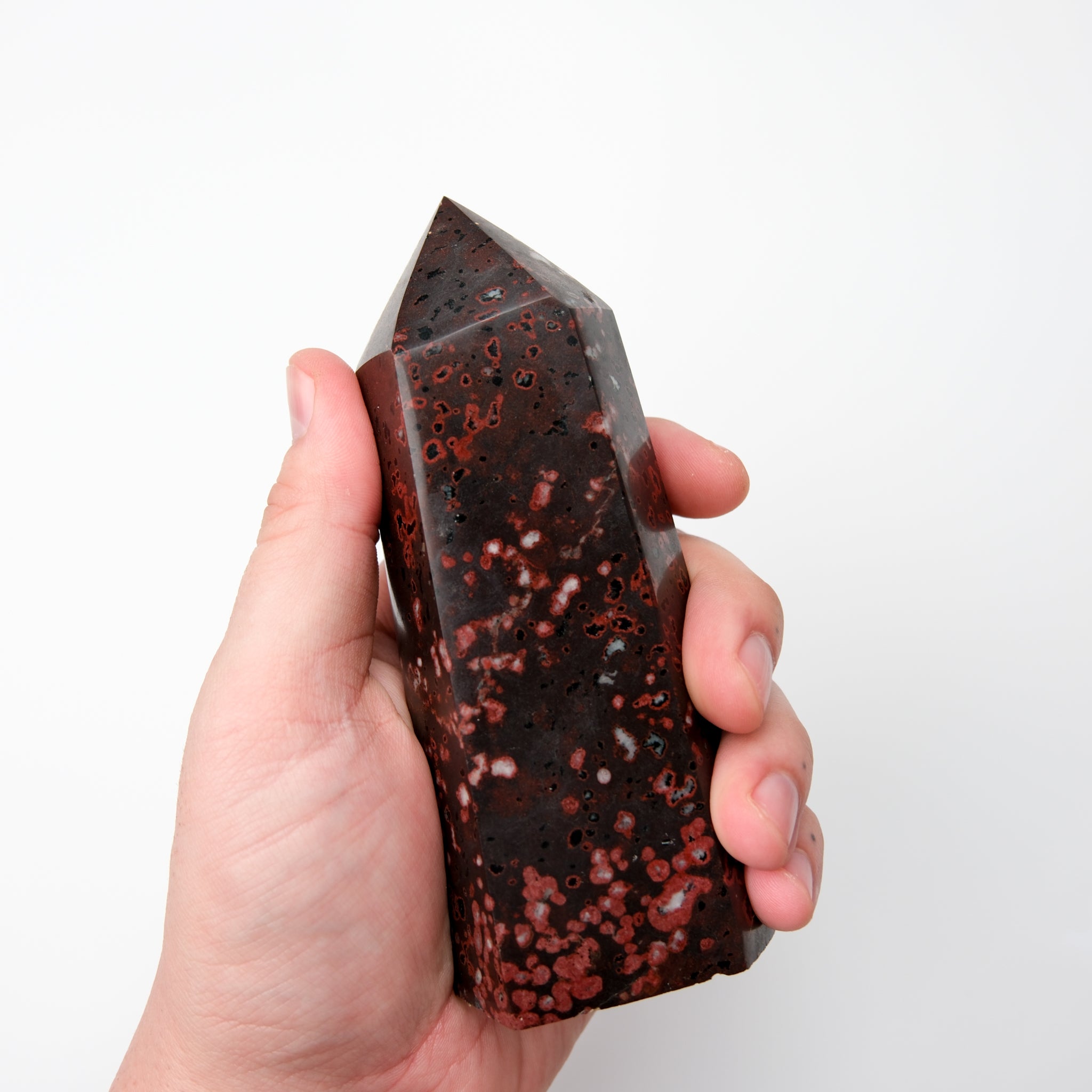 Cinnabar Peridotite pillar sculpture by Noctis Studio showing a tall, polished stone pillar with reddish and green hues.