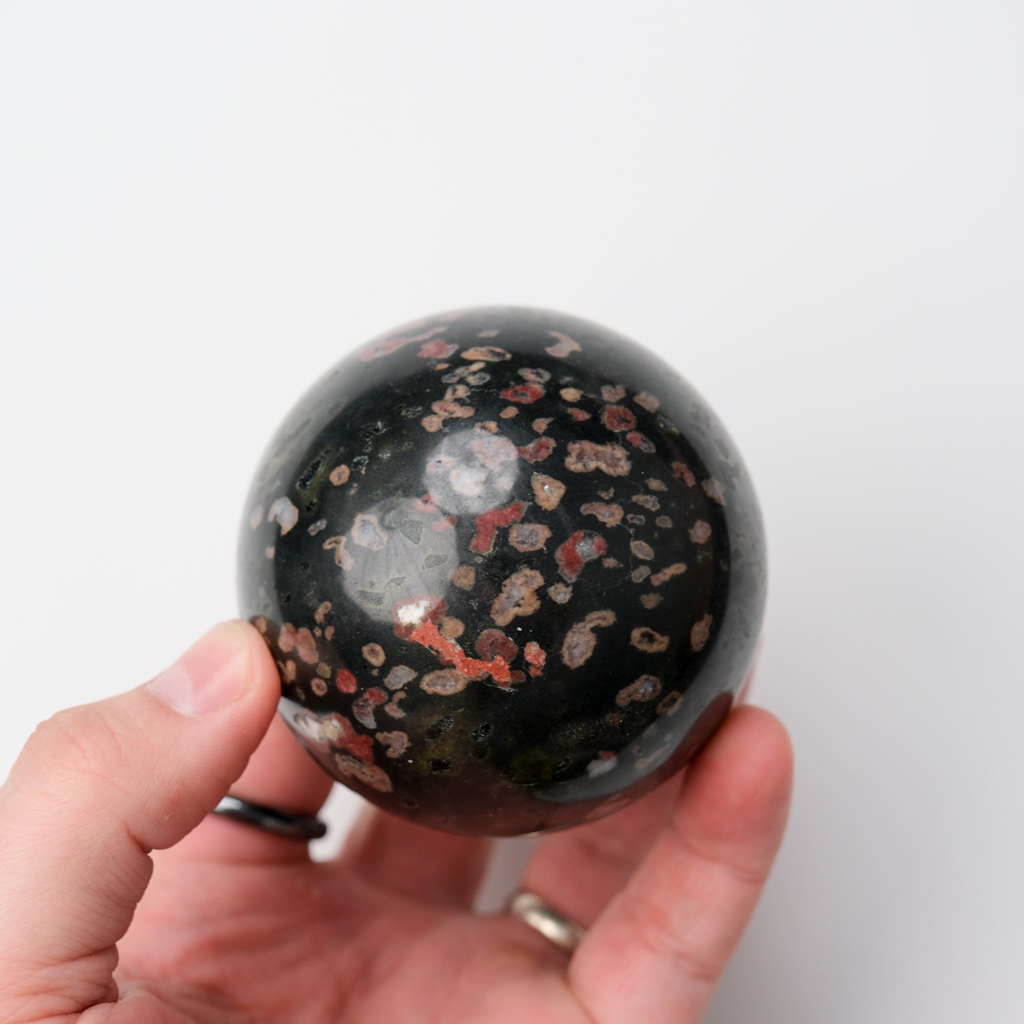 Cinnabar Peridotite sphere from Noctis Studio, smooth polished stone with rich reddish-brown and green mineral patterns.
