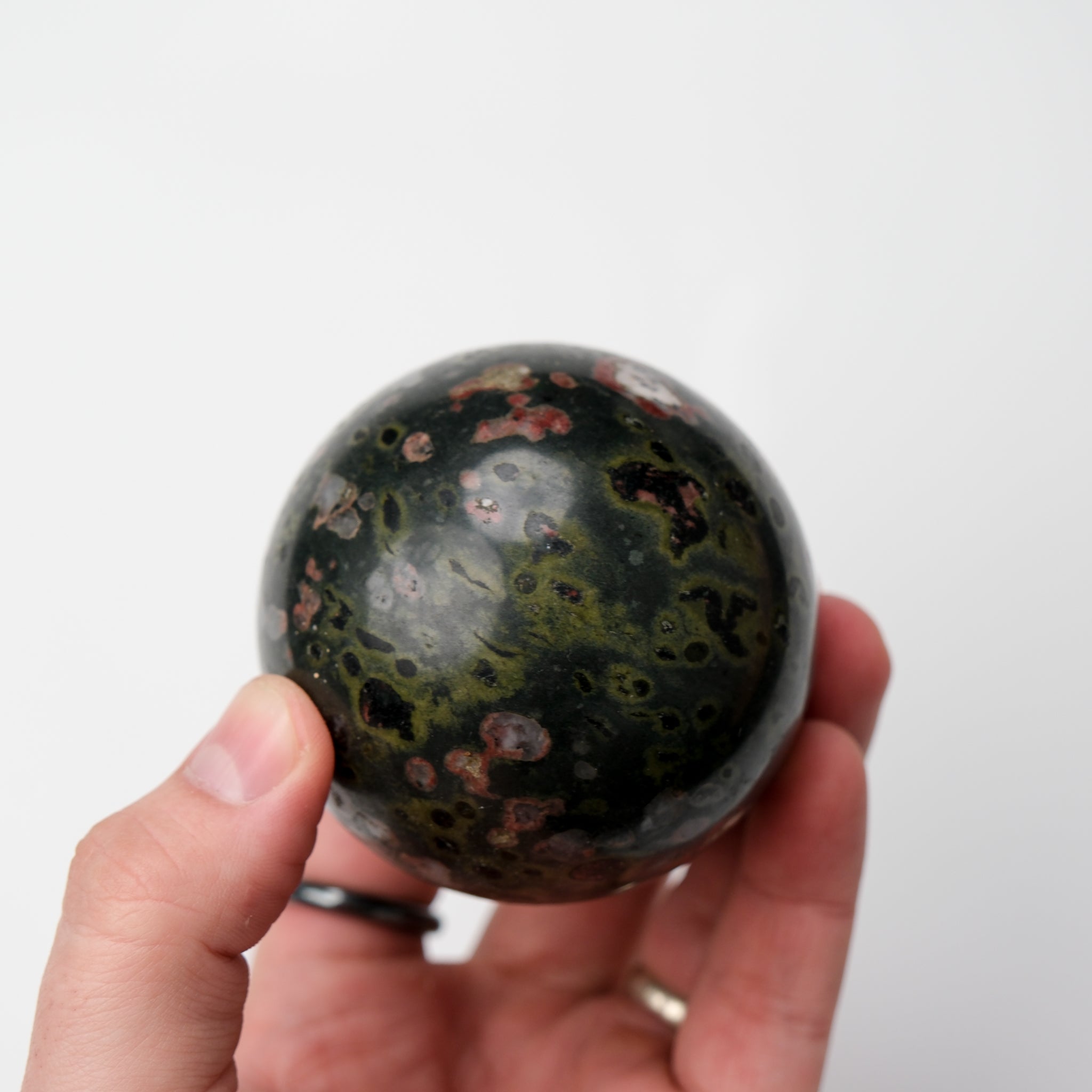 Cinnabar Peridotite sphere from Noctis Studio, showing rich reddish and green mineral patterns with polished smooth surface.