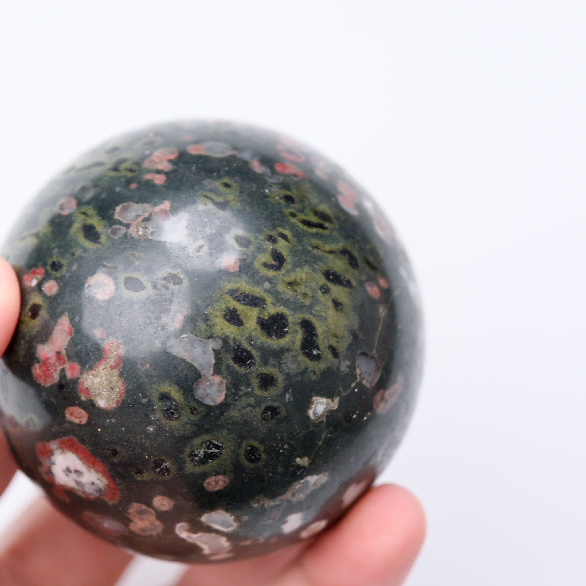 Cinnabar Peridotite sphere from Noctis Studio showcasing a smooth, polished natural mineral with rich red and green hues.