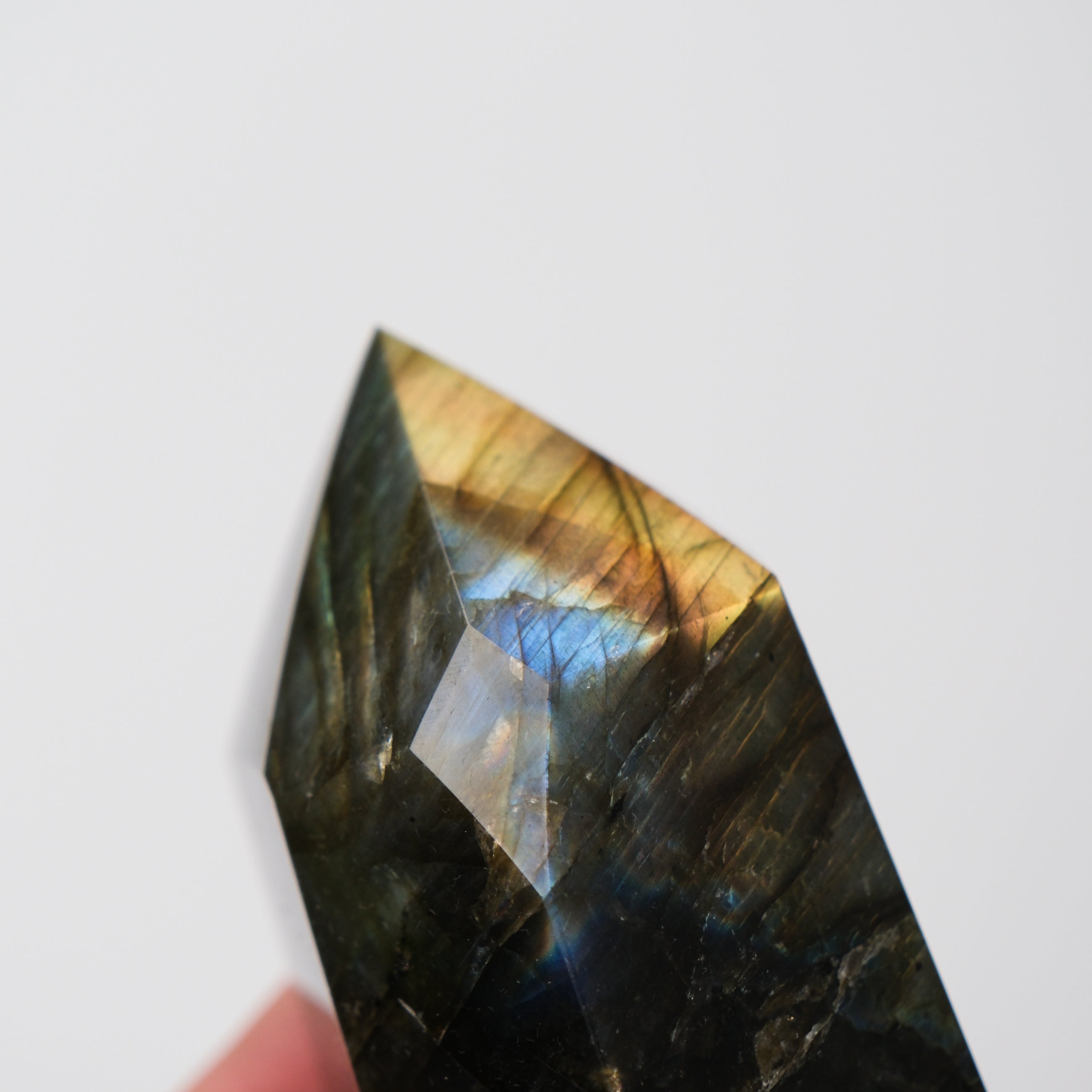 Labradorite pillar sculpture by Noctis Studio, smooth polished stone with iridescent flashes, displayed on a neutral surface.