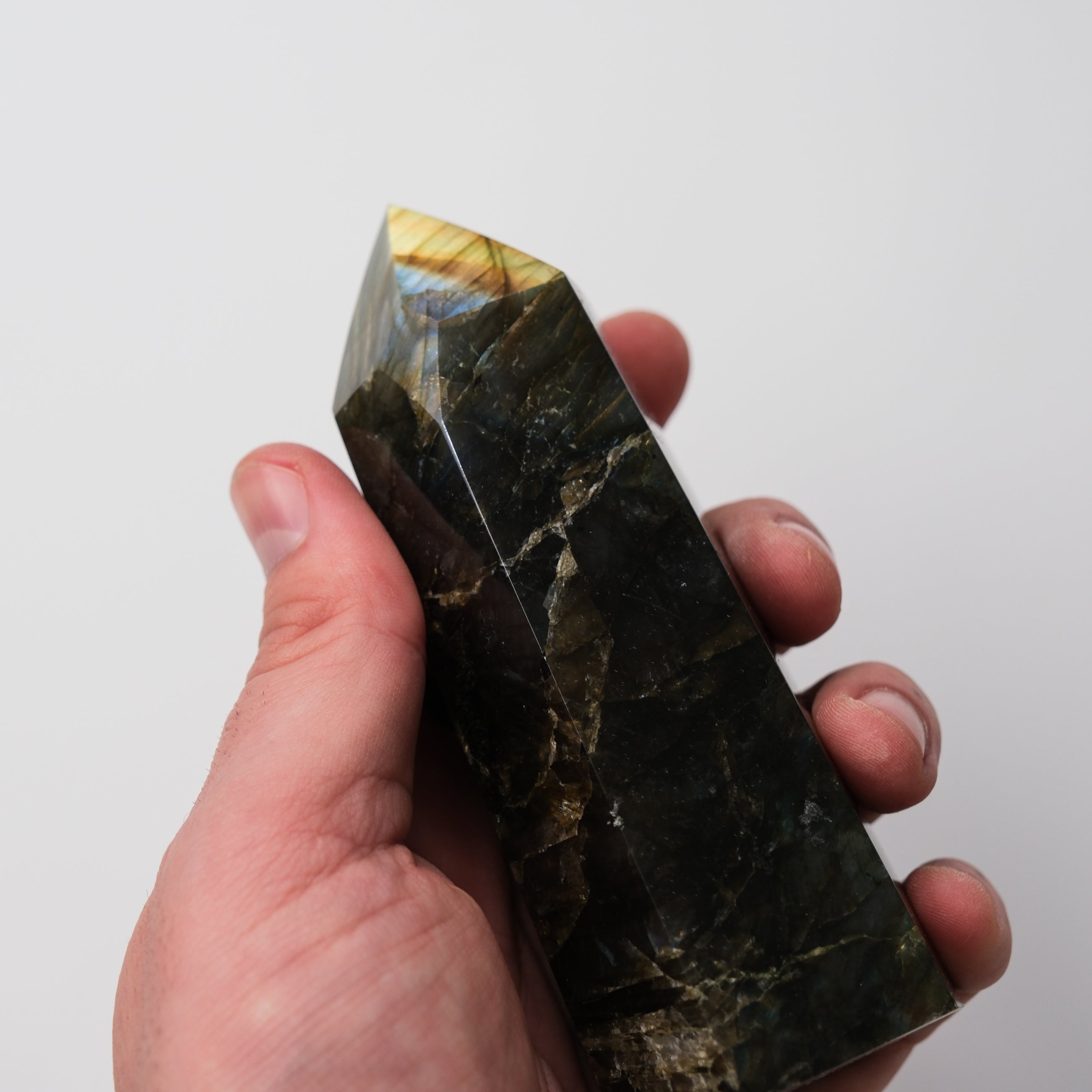 Labradorite pillar sculpture by Noctis Studio, polished mineral with iridescent blue and green flashes, standing on a wooden base.