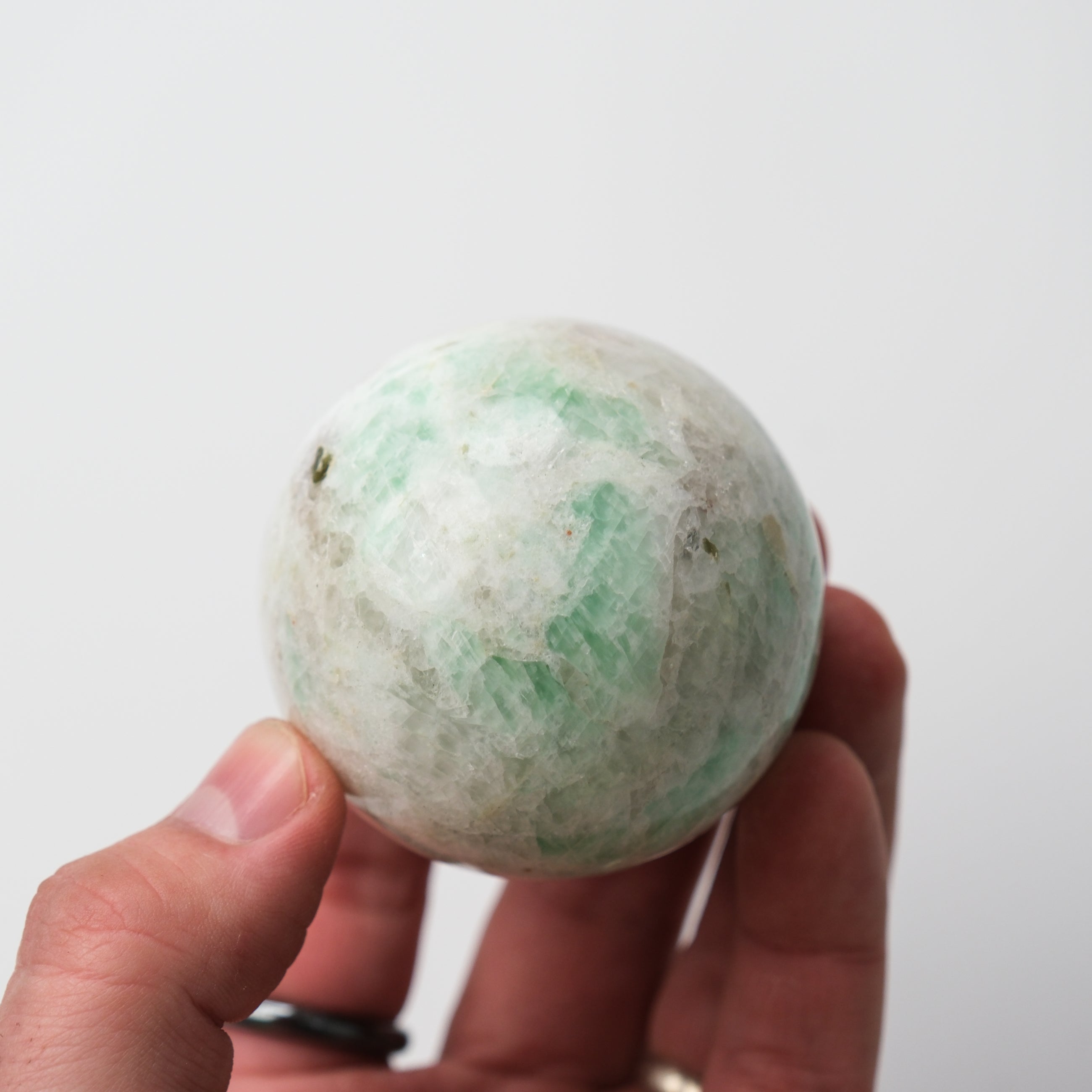 Green moonstone sphere by Noctis Studio, smooth polished gemstone with a luminous, iridescent surface on a neutral background.