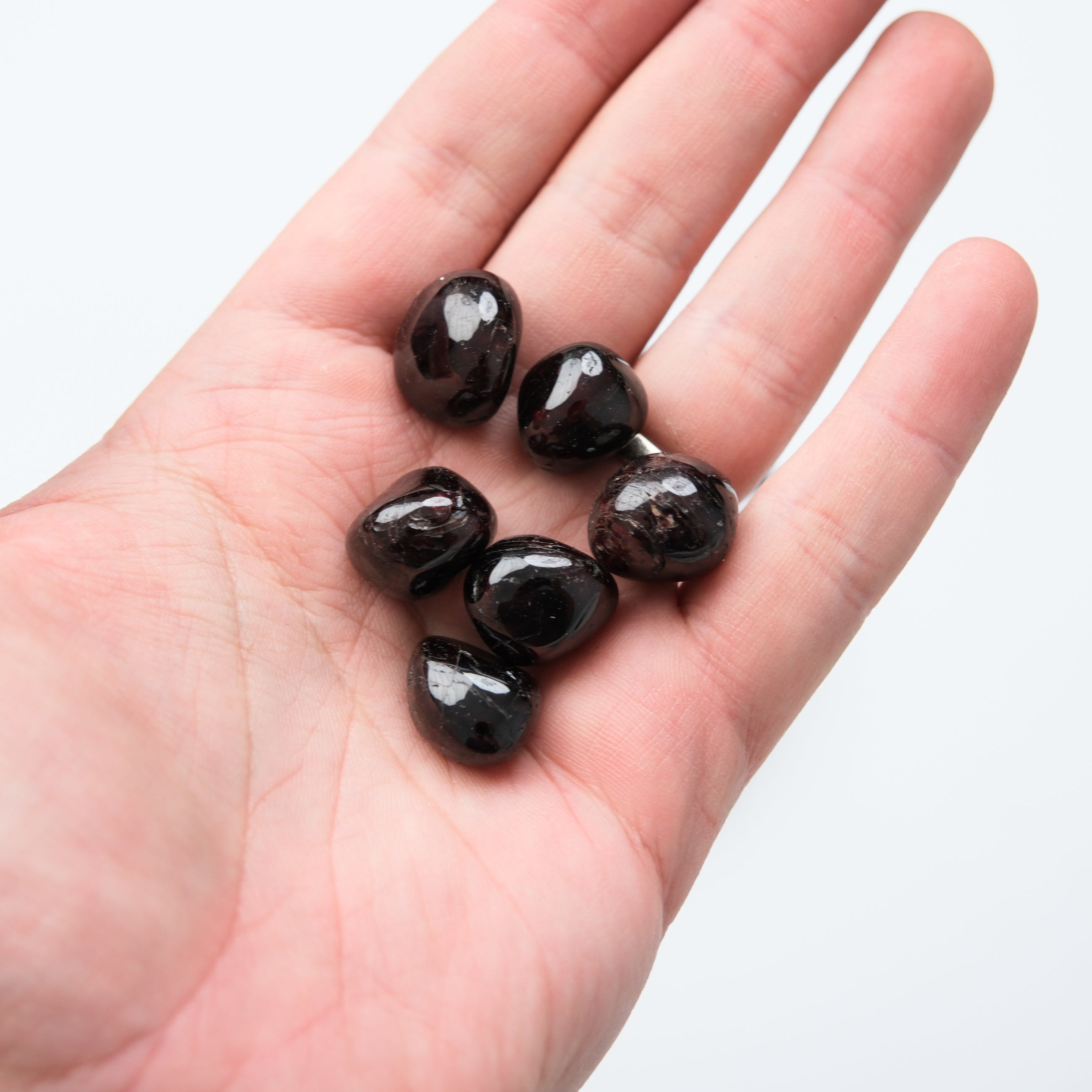 Garnet tumble stone from Noctis Studio showing a polished red gemstone with natural facets and smooth surface.