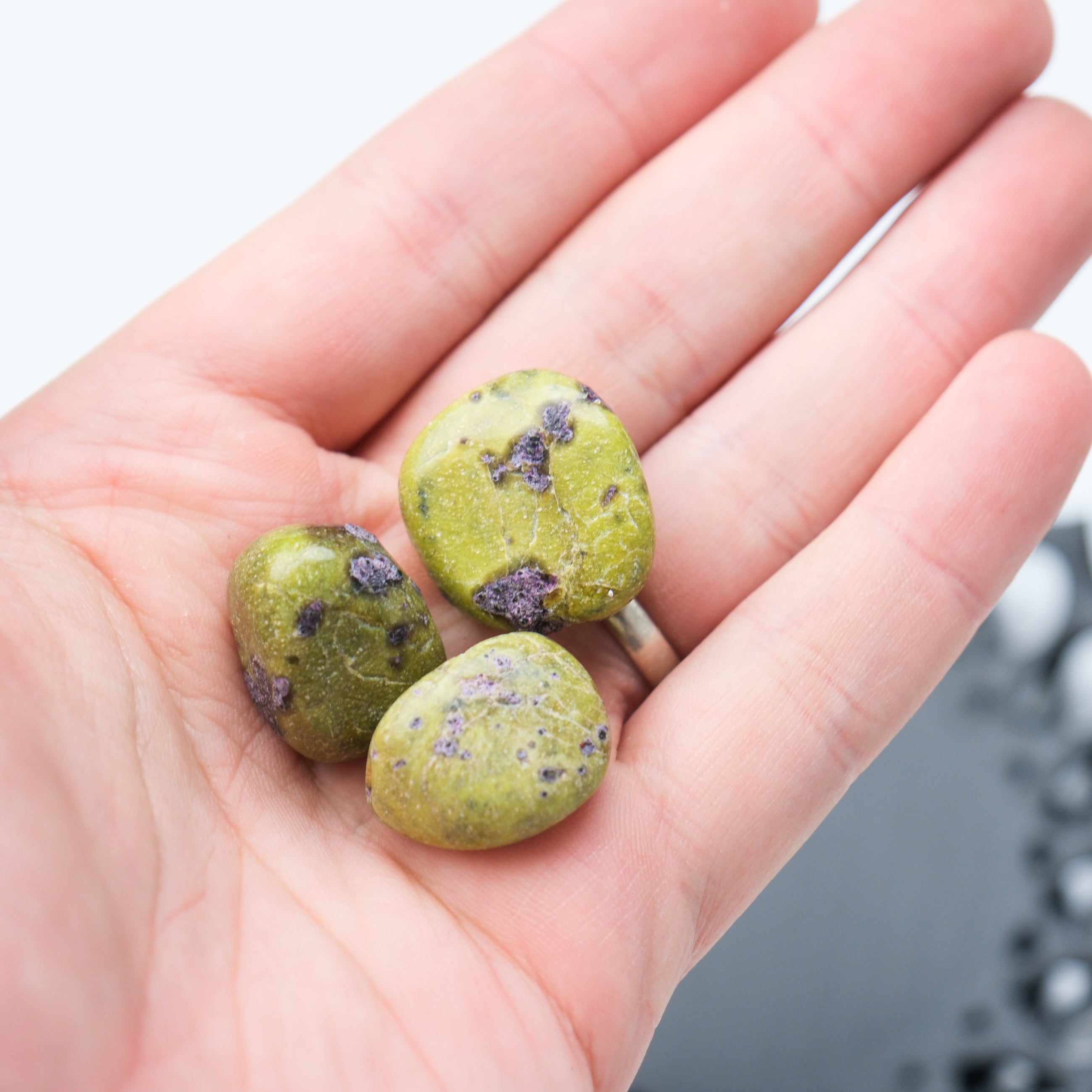 Atlantisite tumble stone by Noctis Studio showing green and purple mineral patterns on a smooth polished surface.