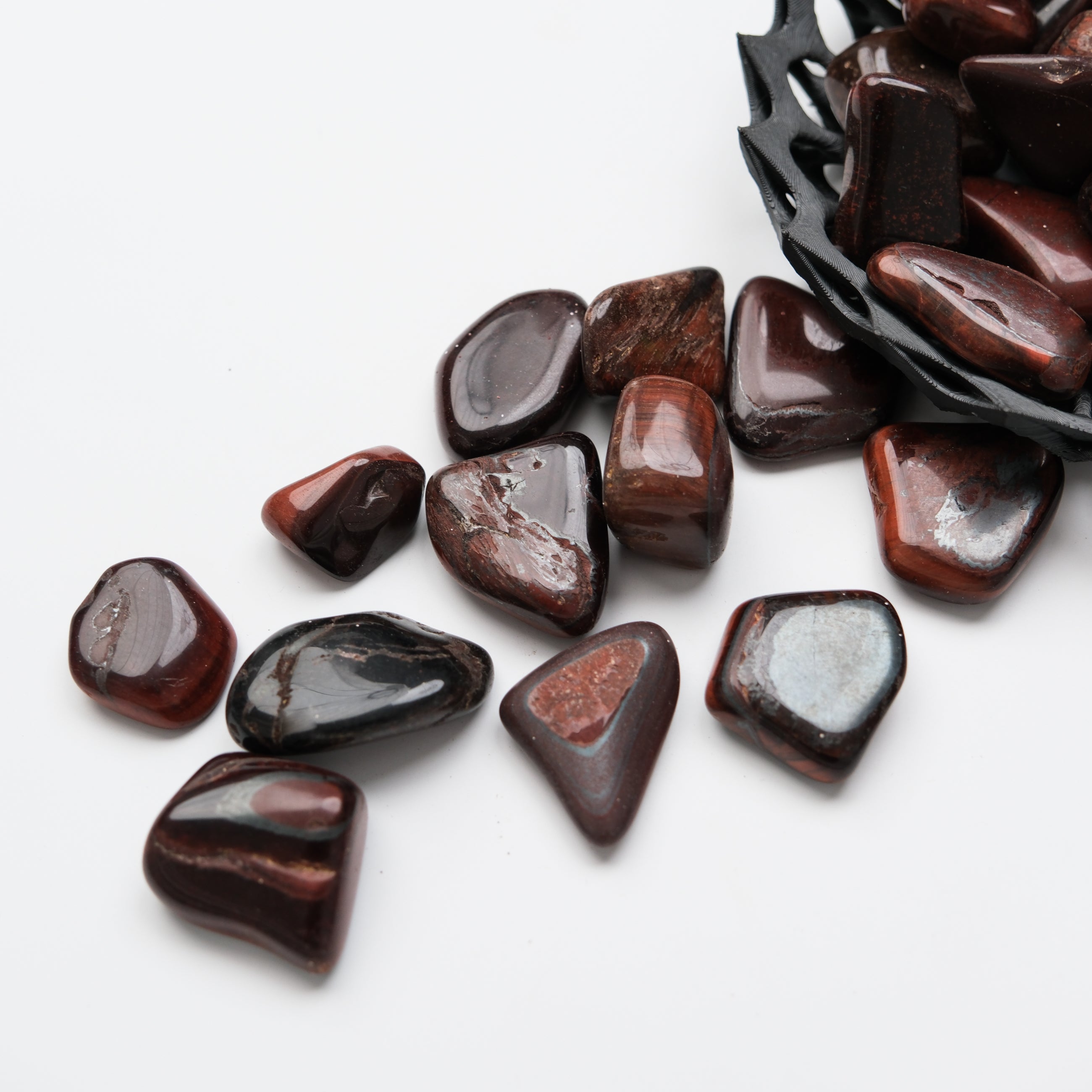 Red Tigers Eye tumble stone from Noctis Studio showing polished, smooth gemstone with rich red and gold hues in a close-up shot.