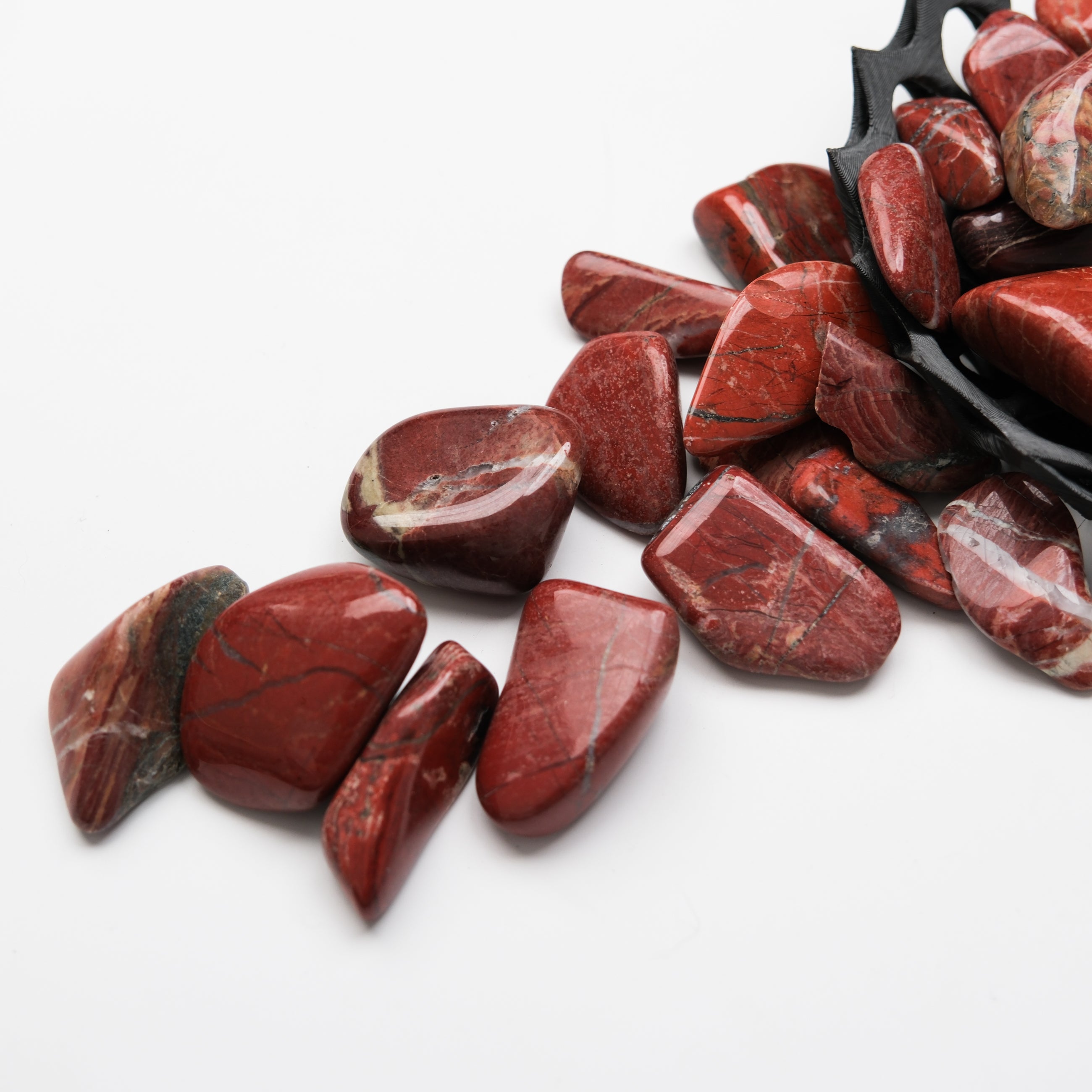 Red Jasper tumble stone from Noctis Studio, showing a polished, vibrant red gemstone with natural patterns and smooth surface.