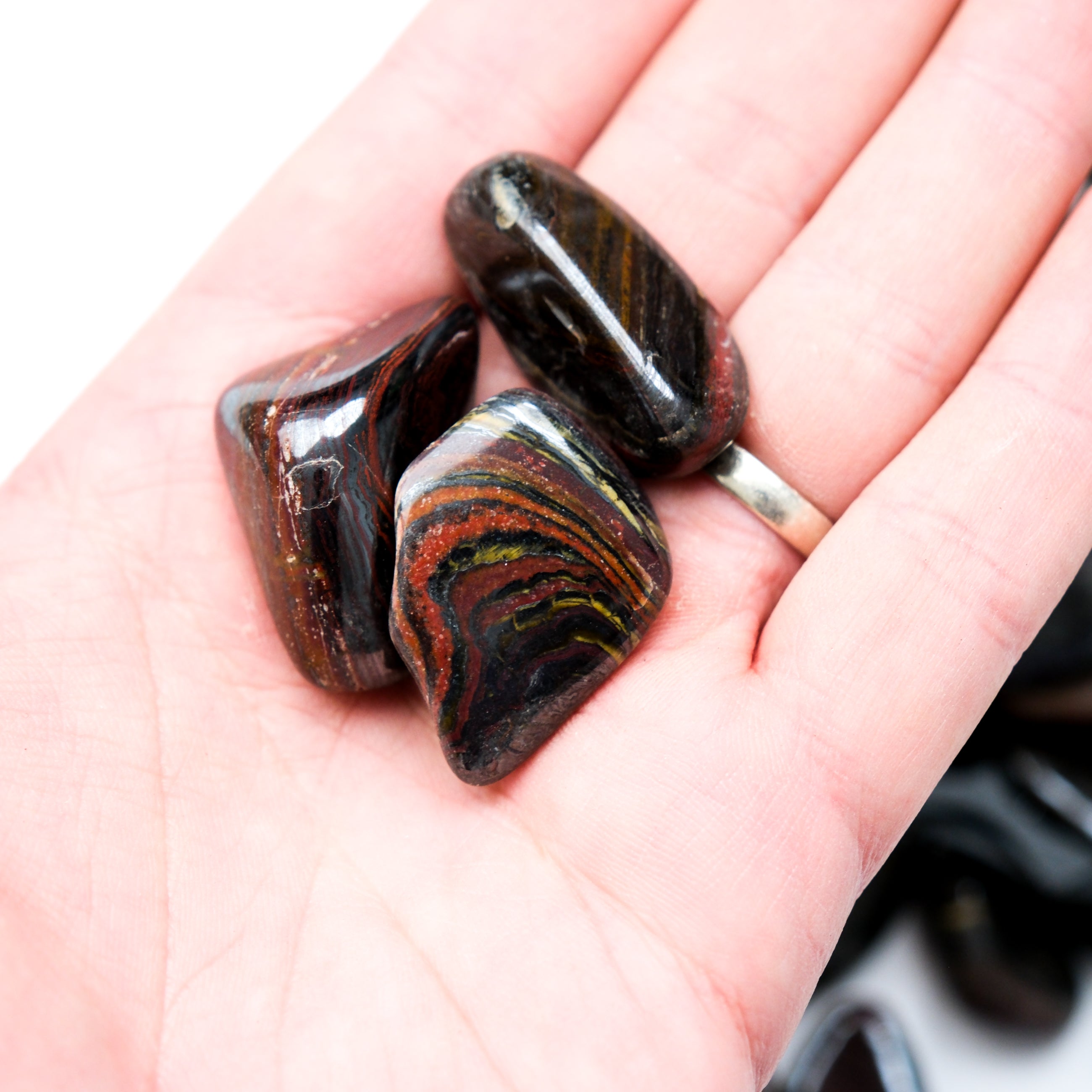 Red Tigers Iron Tumble Stone from Noctis Studio, smooth polished gemstone with vibrant red and black tiger stripe patterns.