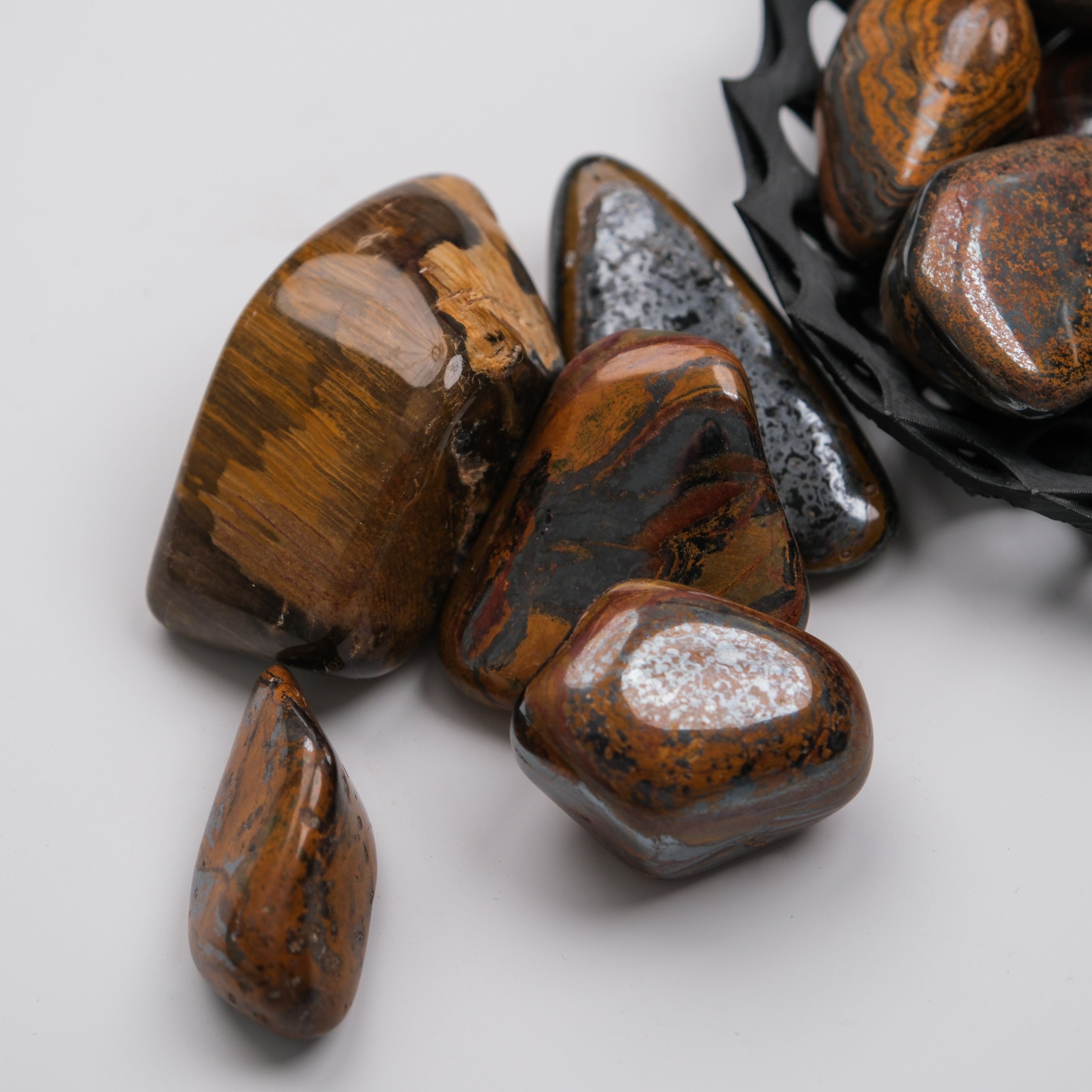 Tigers Iron Tumble Stone from Noctis Studio showing polished, smooth surface with characteristic tiger's eye pattern in natural light.