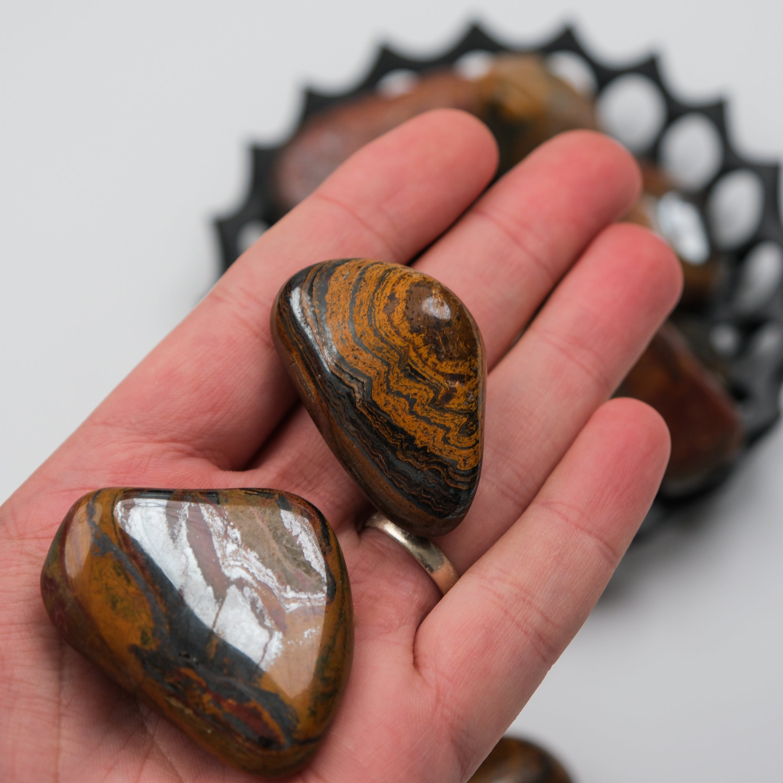 Tigers Iron Tumble Stone from Noctis Studio showing a polished, rounded stone with distinctive tiger’s eye coloration.