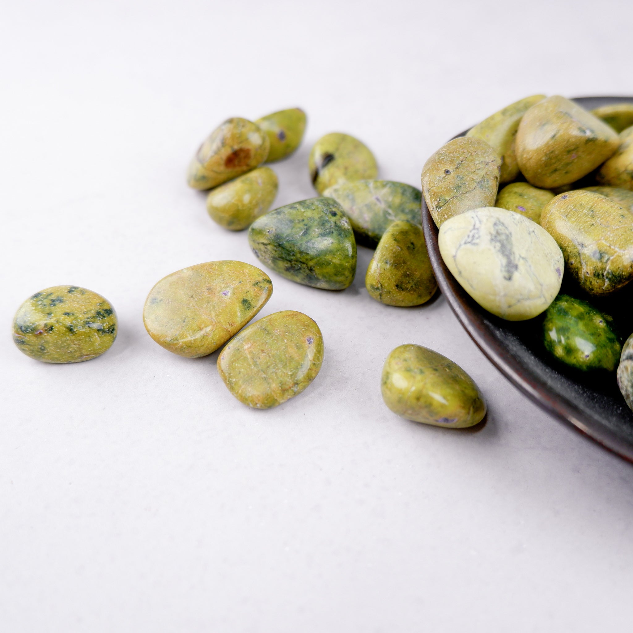 Atlantisite tumble stone from Noctis Studio showing vibrant green and purple mineral patterns on a smooth polished surface.