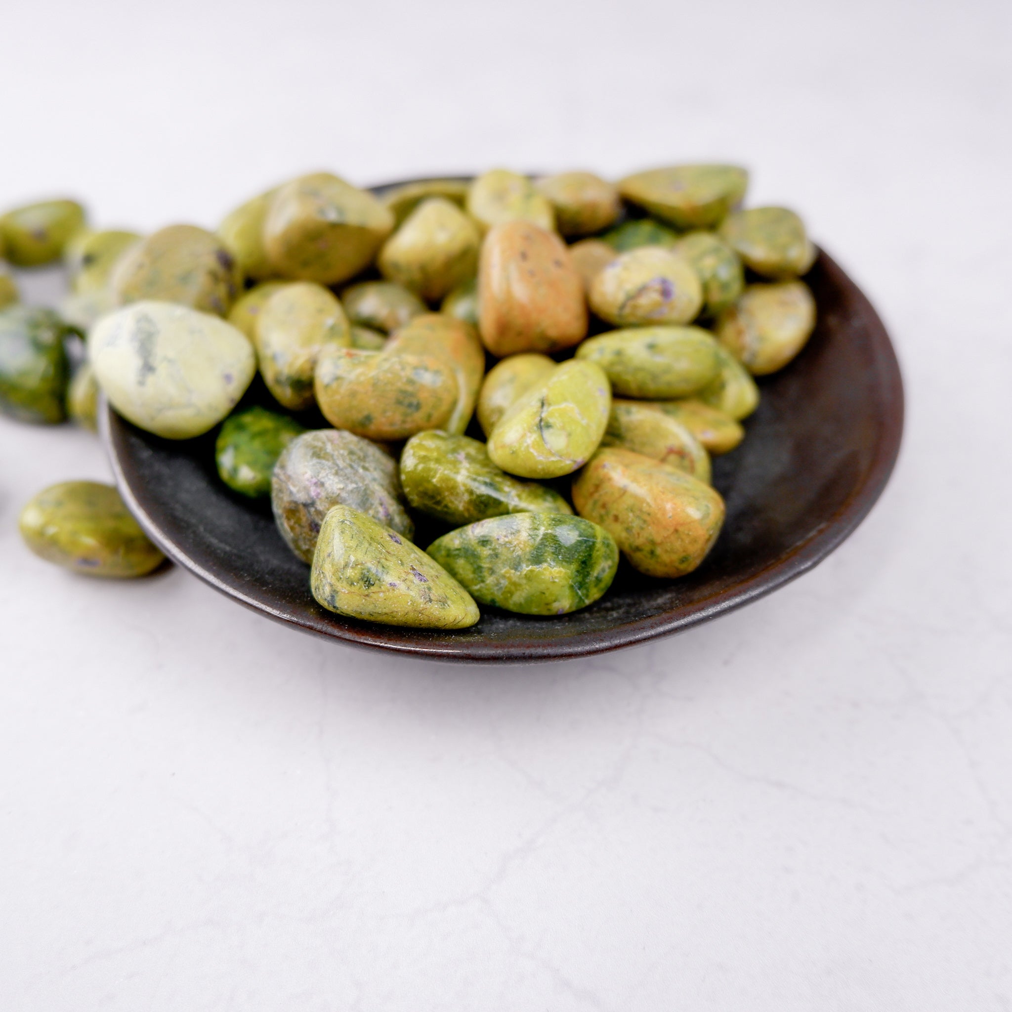 Atlantisite tumble stone from Noctis Studio showcasing vibrant green and purple mineral patterns on a smooth, polished surface.