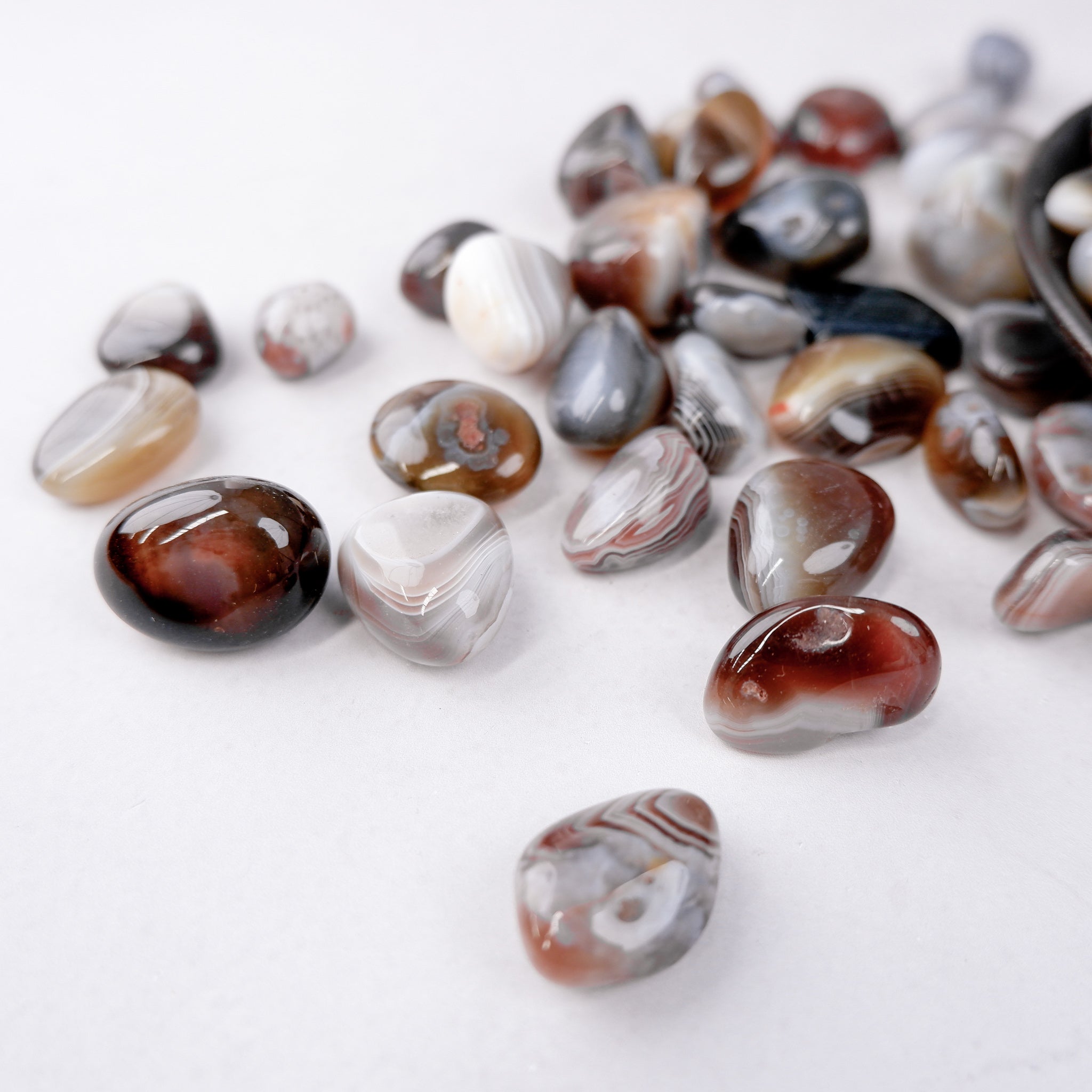 Botswana Agate tumble stone by Noctis Studio showing smooth, polished grey and white banded gemstone on a neutral background.