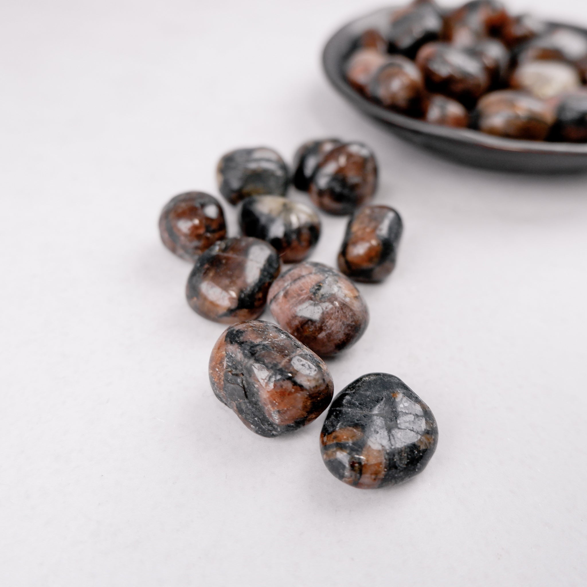Chiastolite tumble stone from Noctis Studio, showing its distinctive cross pattern and dark mineral hues on a smooth polished surface.