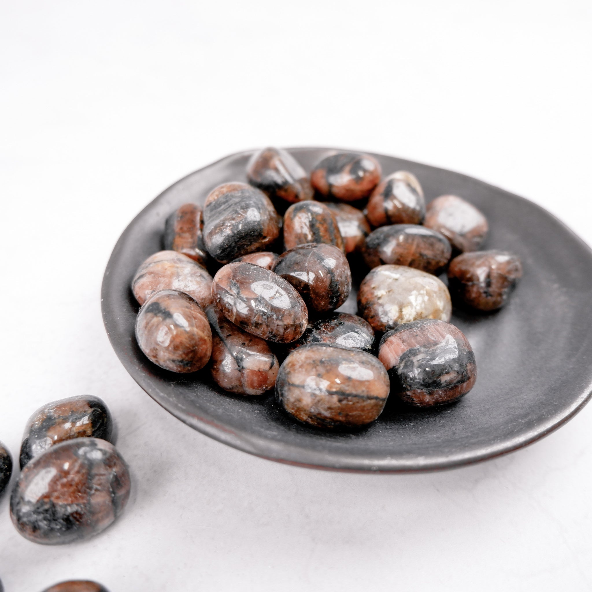 Chiastolite tumble stone by Noctis Studio, showing a polished dark mineral with distinctive cross-shaped inclusions.
