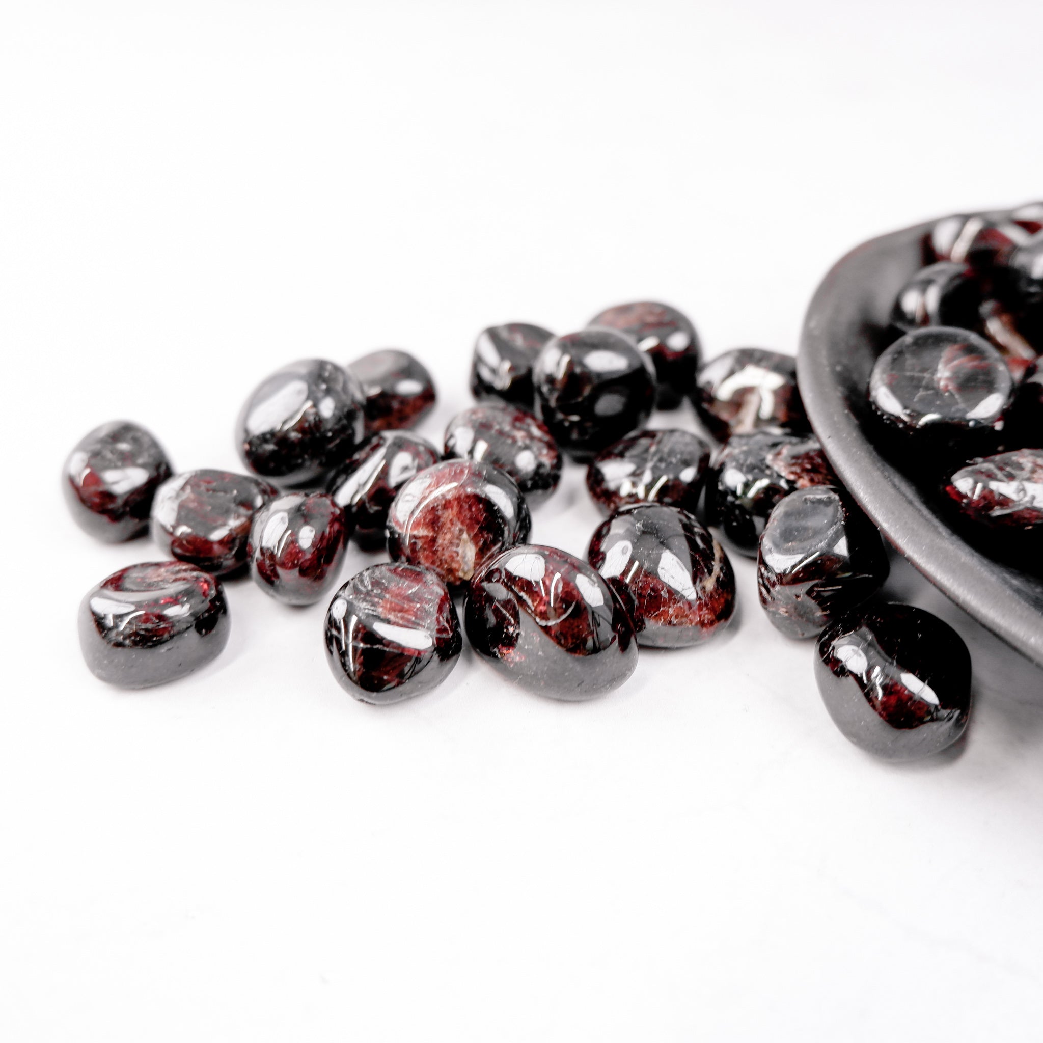 Garnet tumble stone from Noctis Studio, showcasing a polished red gemstone with a smooth, rounded surface on a white background.