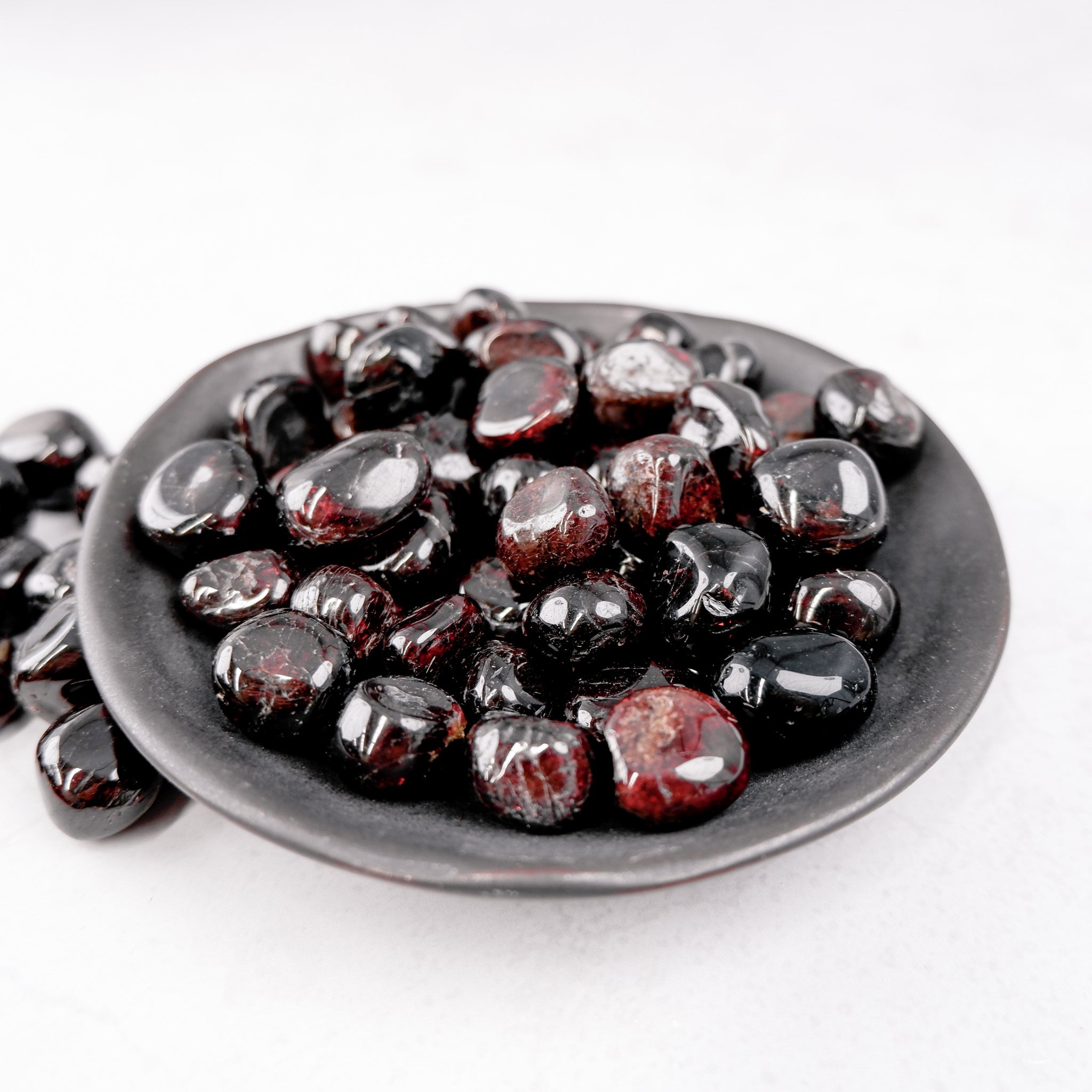Garnet tumble stone from Noctis Studio, showing polished red gemstone with smooth, rounded surface on a neutral background.