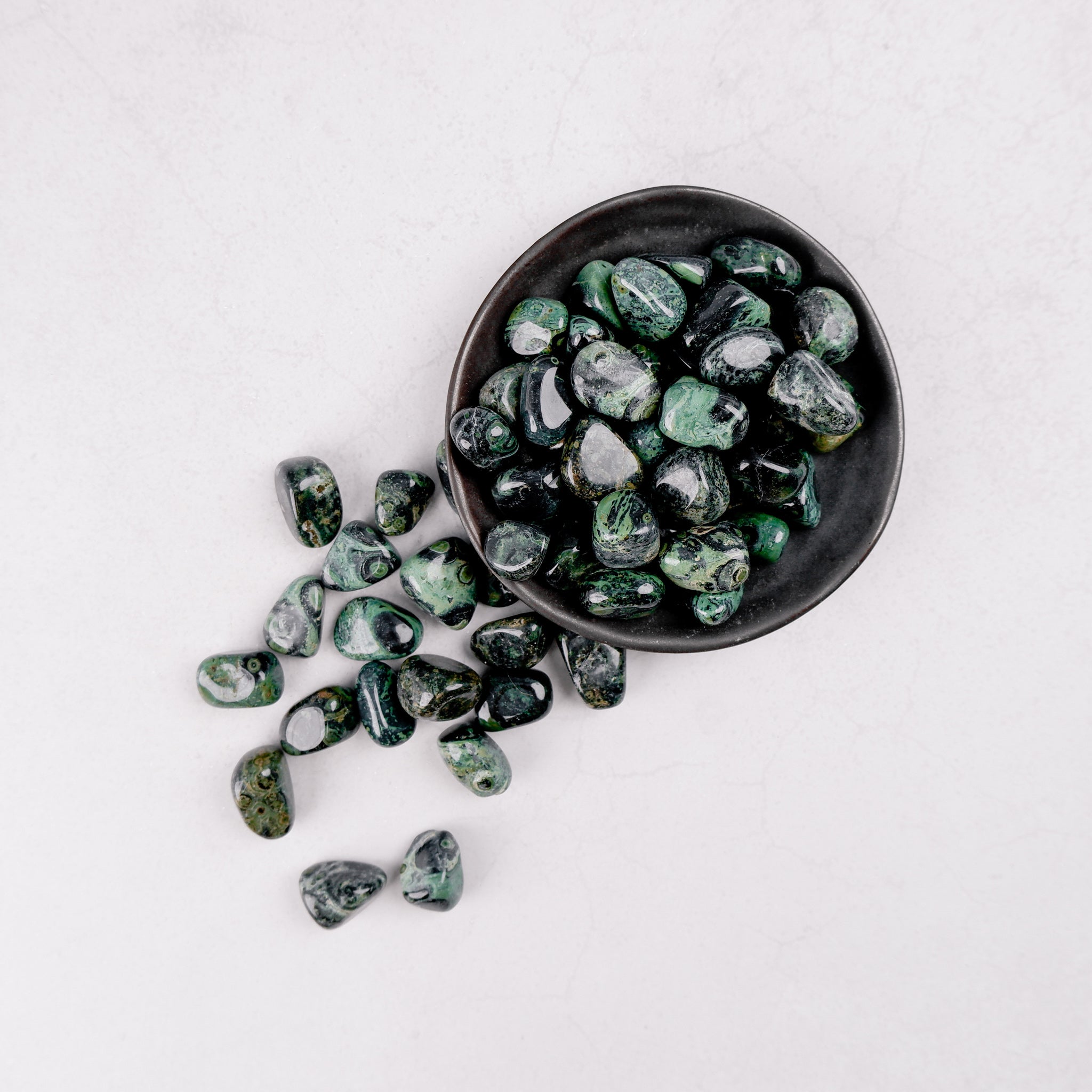 Kambaba Jasper tumble stone from Noctis Studio, showcasing a round, polished stone with green and black swirling patterns.