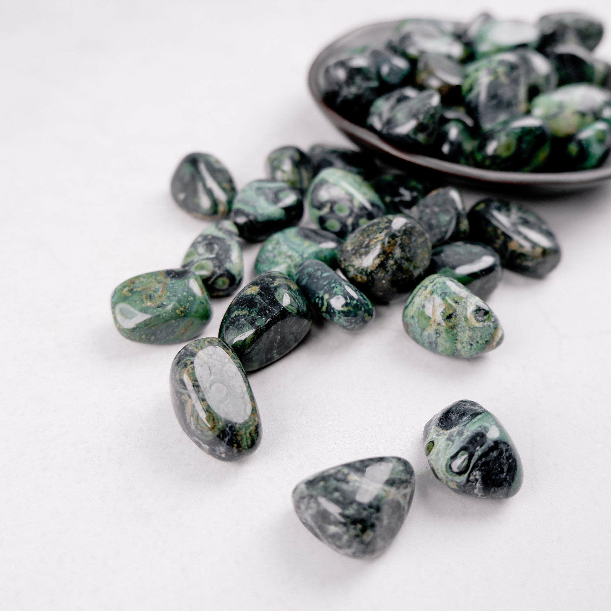 Kambaba Jasper tumble stone from Noctis Studio, showing polished, rounded mineral with green and black swirling patterns.