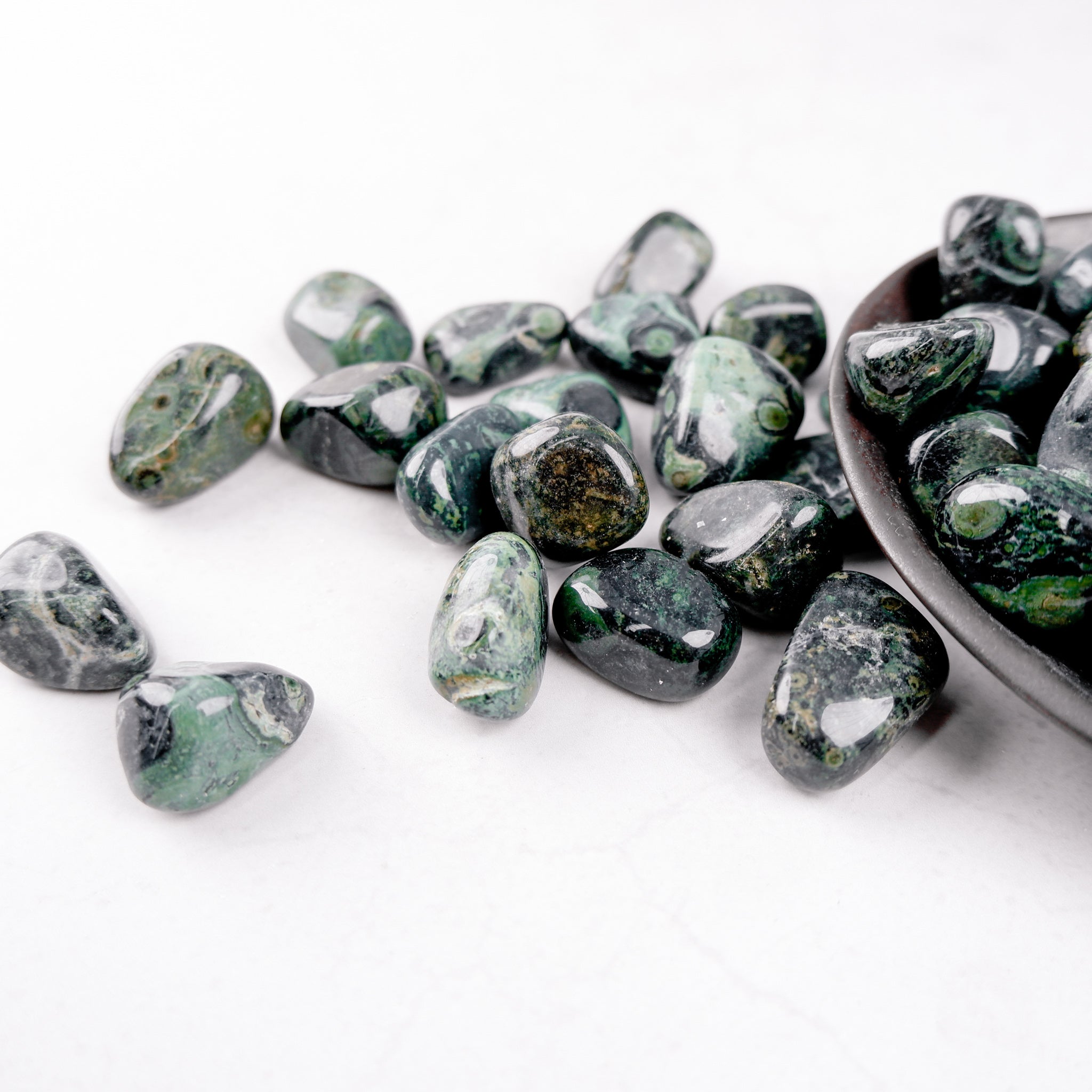 Kambaba Jasper tumble stone from Noctis Studio, showing smooth, rounded natural stone with swirling green and black patterns.