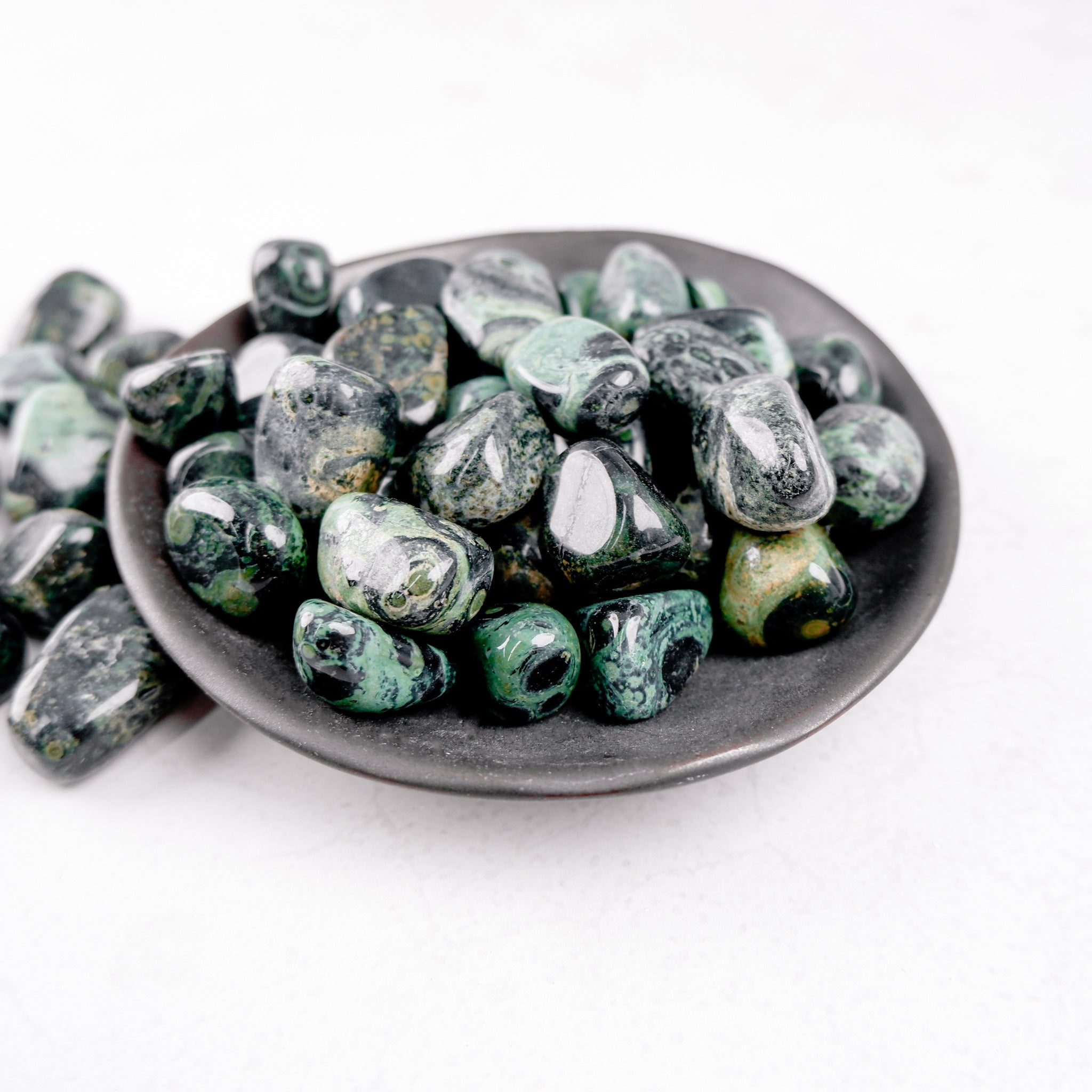 Kambaba Jasper tumble stone from Noctis Studio showing a polished, rounded stone with green and black swirling patterns.