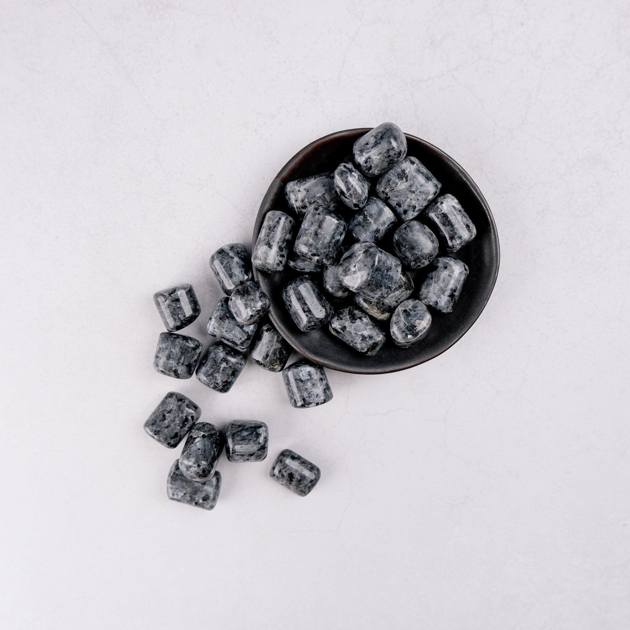 Larvikite tumble stone from Noctis Studio showing a smooth, polished dark gray gemstone with iridescent flash effects.